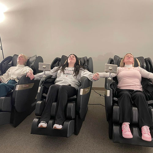 Three female students are reclined in massage chairs.