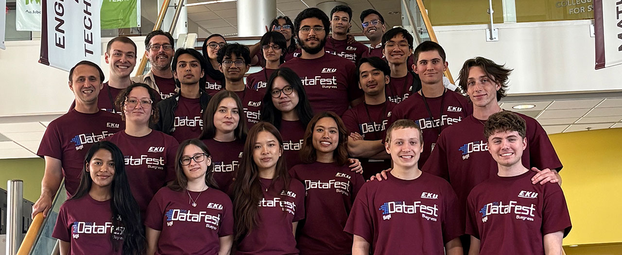 A large group of students wearing EKU t-shirts gather on the stairs in the Science Building for a photo