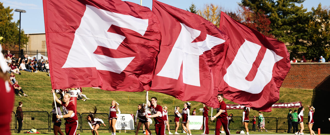 Banner image of cheerleaders carrying EKU flags across the football field