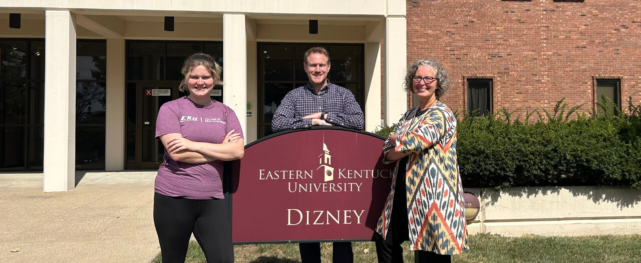 Banner image of three EKU employees standing in front of the sign for the Dizney building