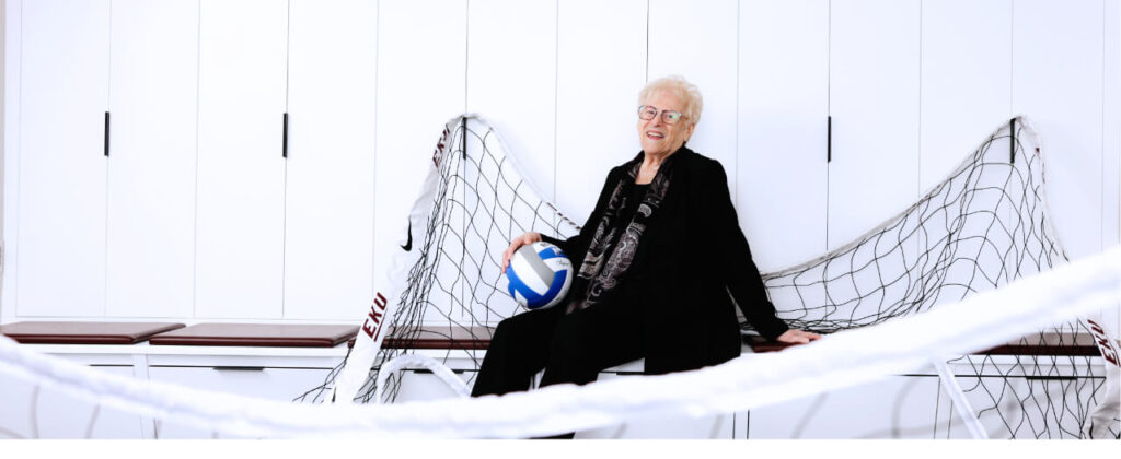 Banner image of Geri Polvino sitting with a ball on a volleyball net